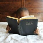Young child reading a Holy Bible indoors, conveying a serene and religious atmosphere.